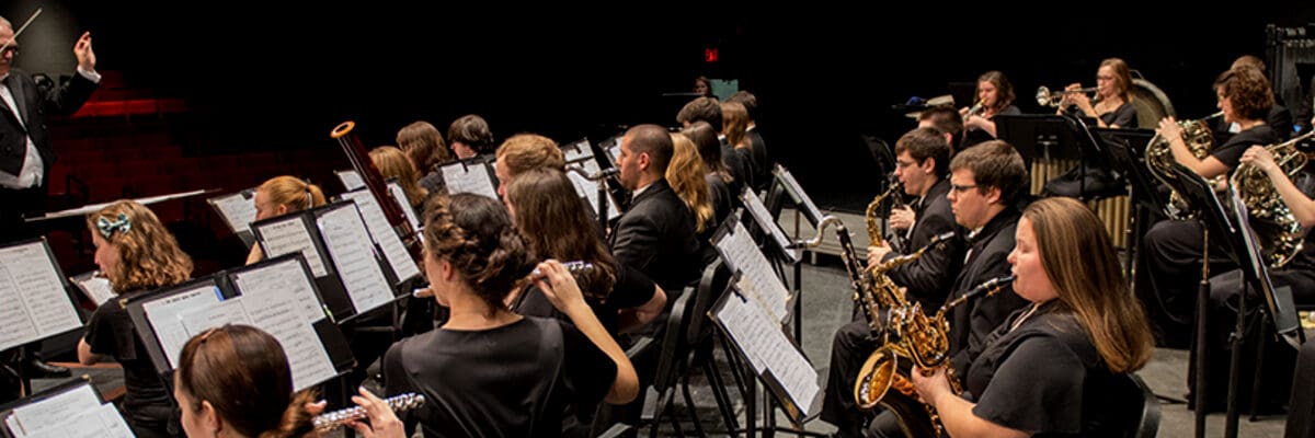 An orchestra sits onstage, ready to perform as the conductor raises his baton