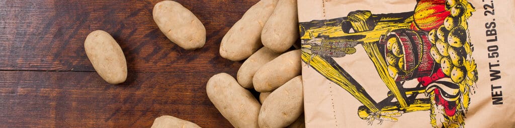 Potatos fall out of a sack and onto a wooden background