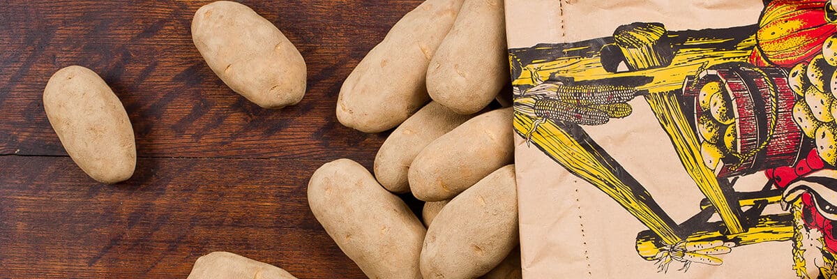 Potatos fall out of a sack and onto a wooden background