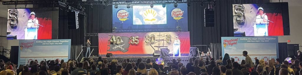 A picture of a live event, the audience packed and watching a presenter onstage