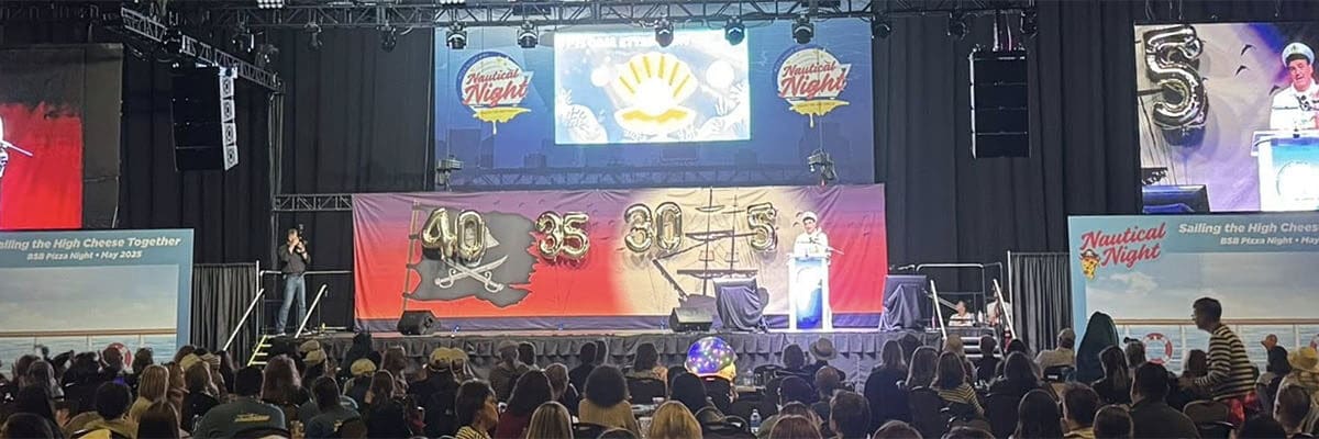 A picture of a live event, the audience packed and watching a presenter onstage