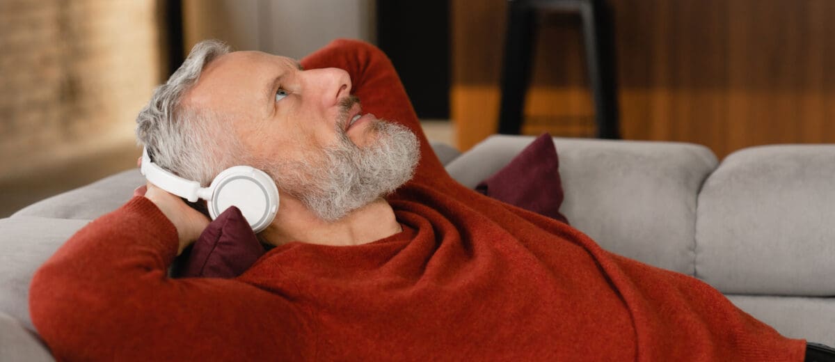 A middle-aged man relaxes on the sofa, wearing headphones